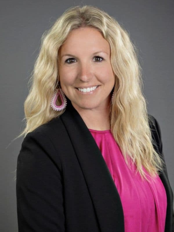 Smiling woman with long blonde hair in a black blazer and pink top.
