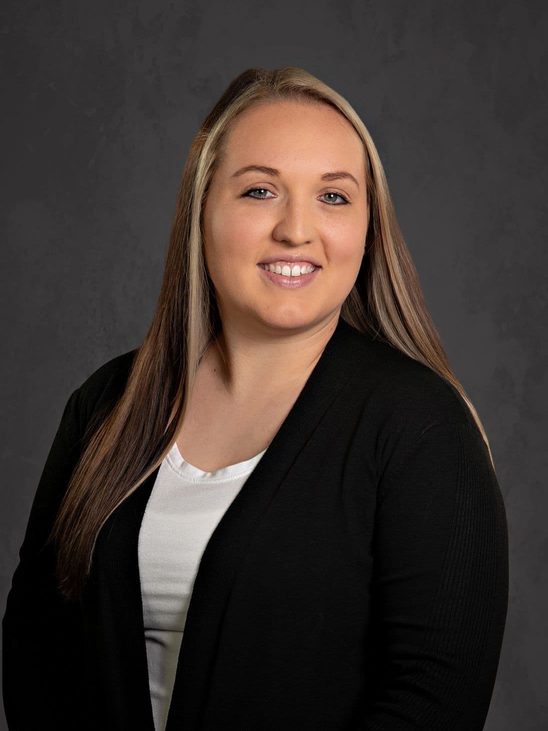 Professional woman with long hair and a black cardigan smiles against a gray backdrop.