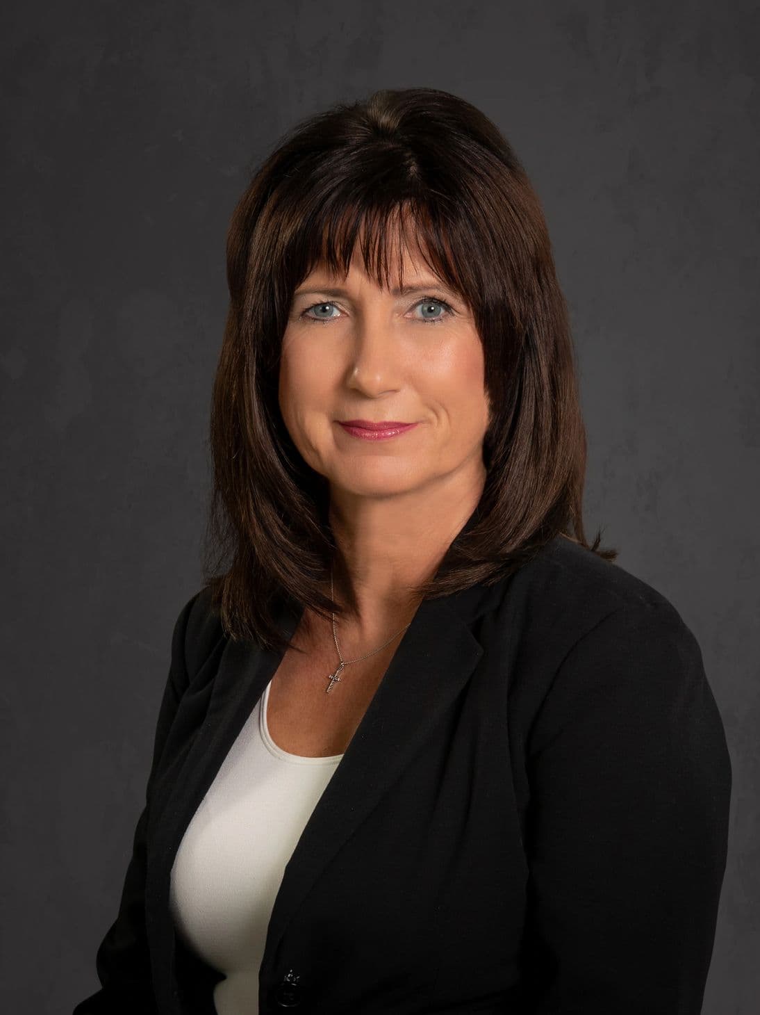 Professional woman in black blazer against dark background.