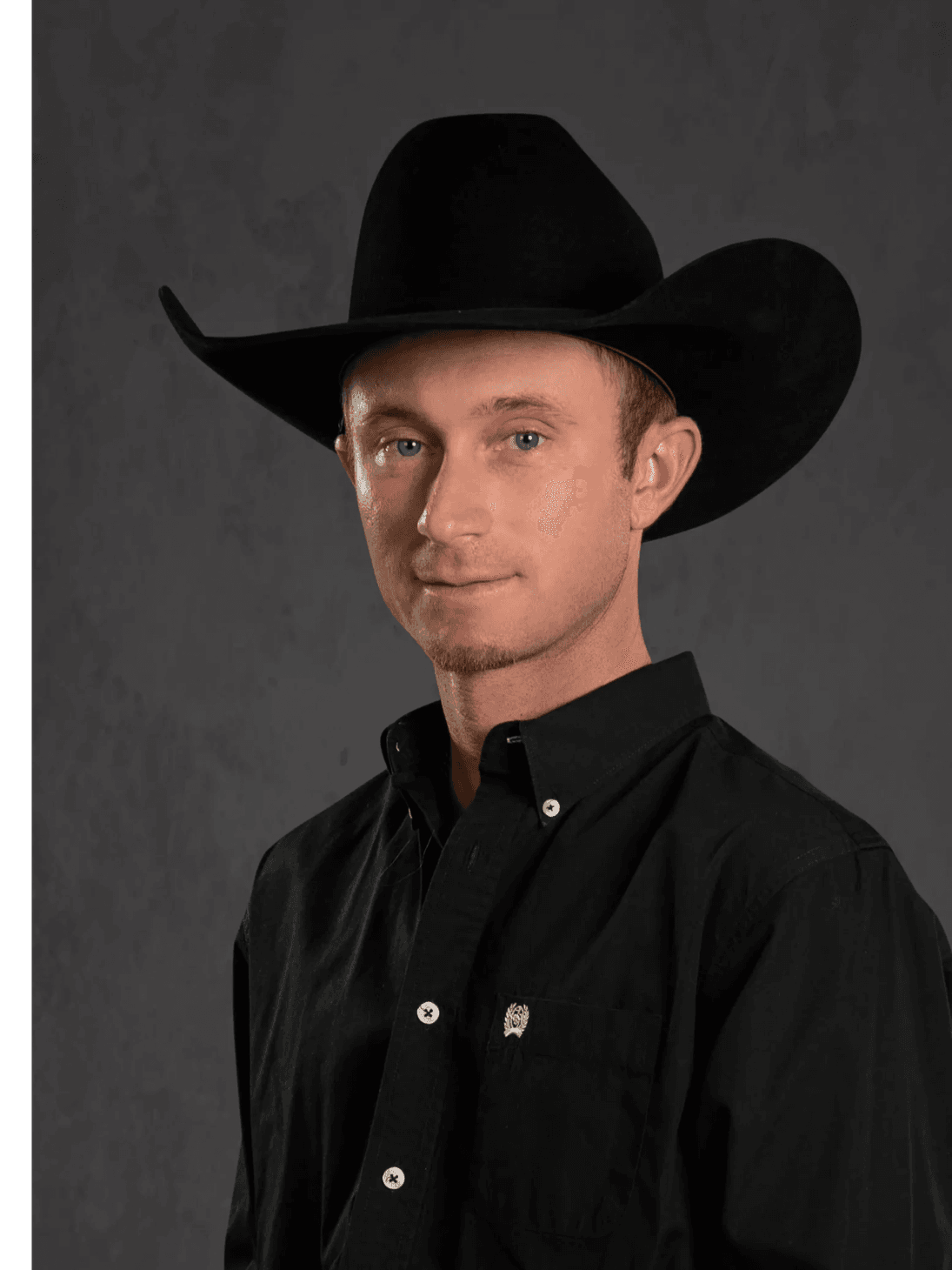A man wearing a black cowboy hat and black shirt poses against a gray background.